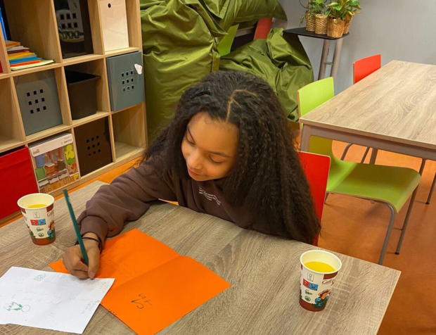 Kindje met krullen schrijft op een oranje papiertje